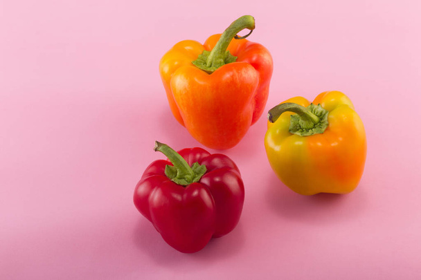 Sweet bellpepper. Two orange-yellow and one red sweet bellpeppers on a pink background. Three pieces. Studio light. Top view - Photo, image