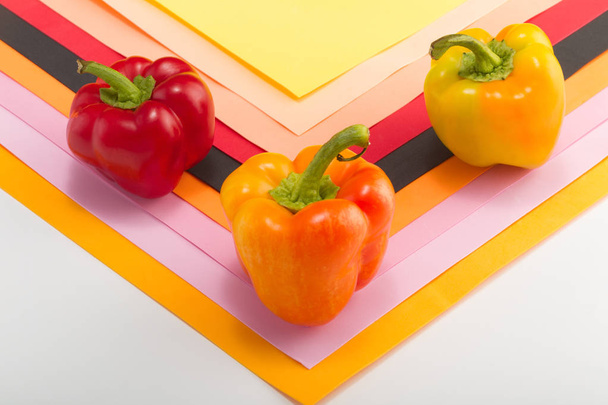 Sweet bellpepper. Two orange-yellow and one red sweet bellpeppers on a colorful background. Pattern. Three pieces. Studio light. Top view - Zdjęcie, obraz