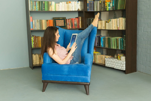 Lidé, vzdělávání a technologie koncept - žena čte digitální tabletu v křesle v knihovně - Fotografie, Obrázek
