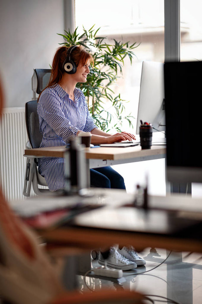 Young businesswoman working in office with headphones - Photo, Image