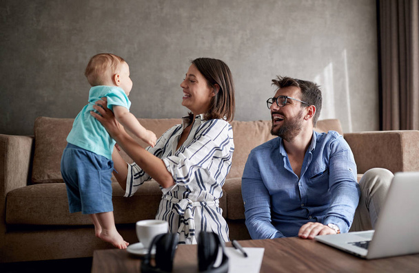 Happy young man and woman with baby working from home using laptop - Photo, image