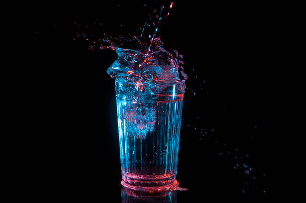 Grande respingo de bebida de vidro vintage em luzes vermelhas e azuis isoladas em um fundo preto
 - Foto, Imagem