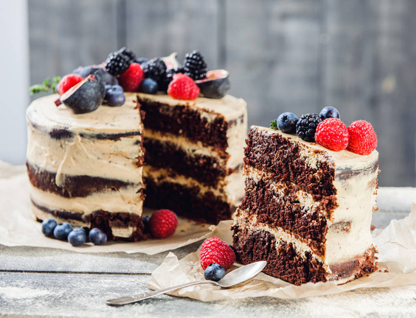 Rustic chocolate cake with buttercream frosting and decorated with berries and figs - Photo, image