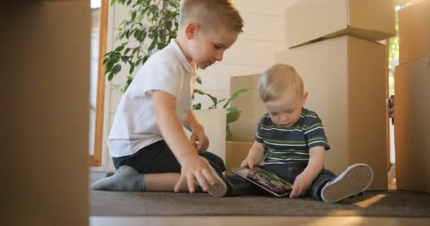 Portrait of two little boys having fun - playing or reading from tablet at their new house. Brothers are interested using and play digital tablet. Education, mortgage, housing and real estate concept. - 映像、動画
