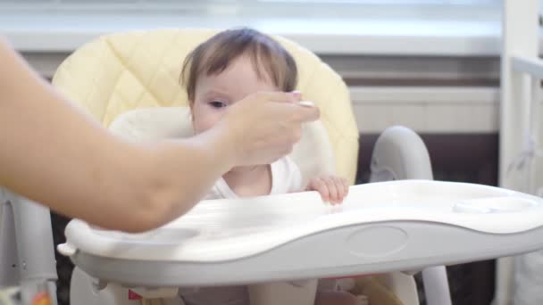 Kind isst Brei vom Löffel, sitzt auf Hochstuhl in Küche. - Filmmaterial, Video