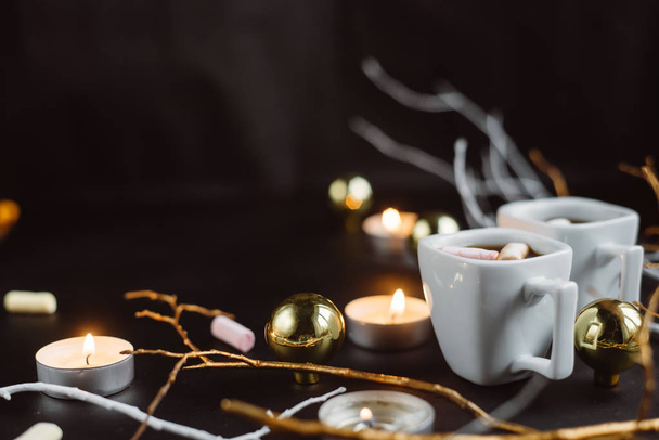 Christmas composition. Two cups of coffee with marshmallows, branches, candles and Christmas toys on a dark background. - Foto, Imagen