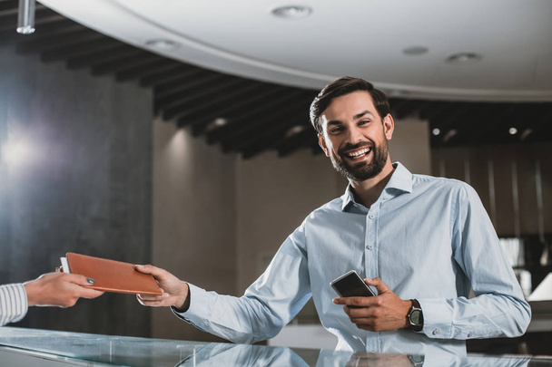 Cheerful man is taking account from receptionist - Photo, Image