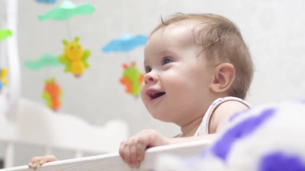 μικρό παιδί στέκεται στα πόδια του σε ένα κρεβάτι μωρού. χαριτωμένο μωρό γέλια - Πλάνα, βίντεο
