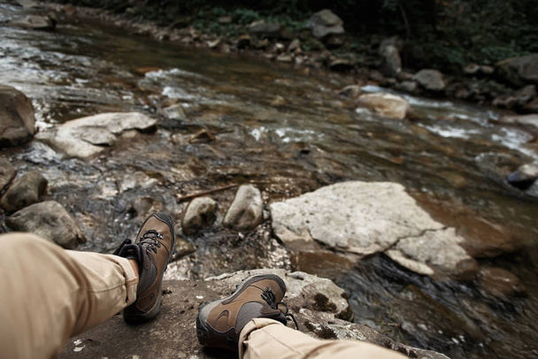 Tired traveler relaxing on the stone near the mountain stream - Foto, afbeelding
