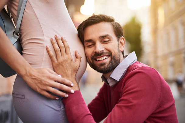 Happy bearded man listening to belly of his pregnant wife - Фото, зображення