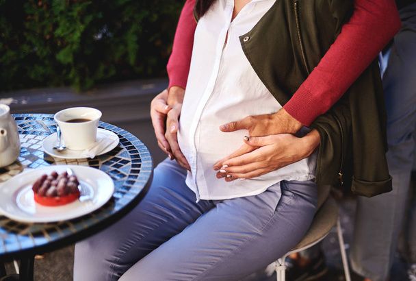 Expectant parents touching lady tummy while she sitting at the table - Photo, image