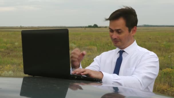 boldog üzletember, kék és fehér ing szerkezet-ban mező, a számítógép a tetőn az autó. - Felvétel, videó