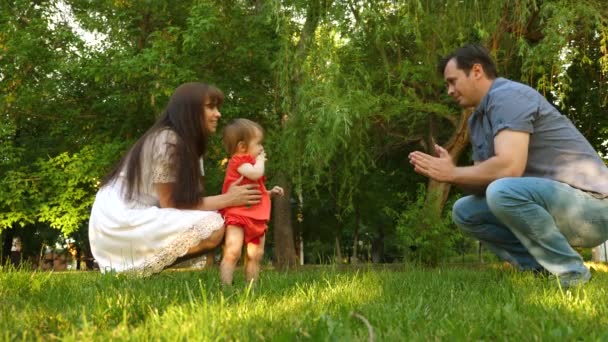 Baby neemt eerste stappen met behulp van pappa en mamma op gazon gras. - Video