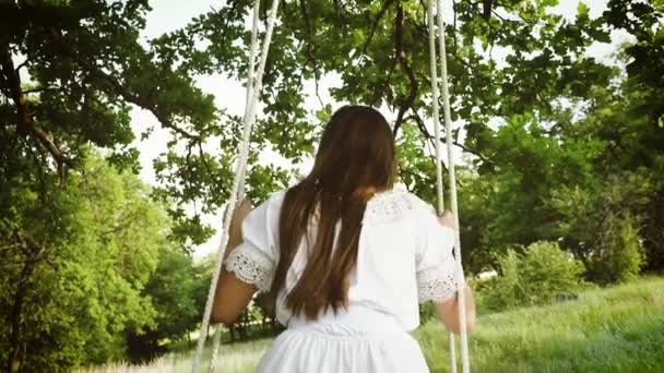 Девушка с длинными волосами качается на качелях в летнем парке. Медленное движение
. - Кадры, видео