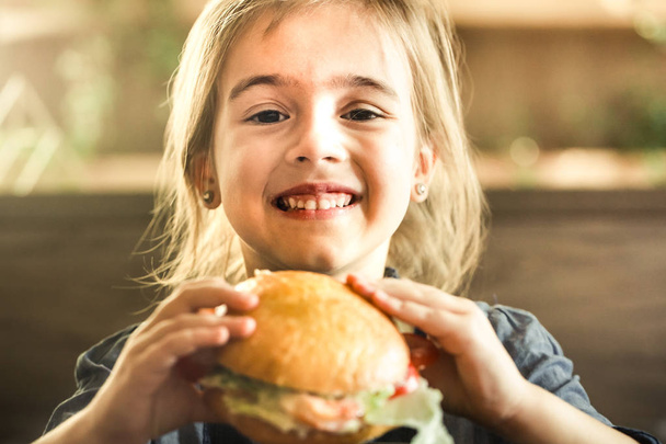Pieni söpö tyttö syö voileipää kahvilassa, käsite lasten pikaruokaa ateria
 - Valokuva, kuva