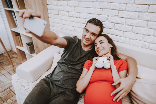 Selfie. Husband and Pregnant Wife. Relaxation. Sit. Together on Couch. Love Each Other. Home. Happy Together. Motherhood. Tenderness. Resting. Happiness. Birth. Parenthood. Sweet. Sofa. Domestic Life. - Photo, image
