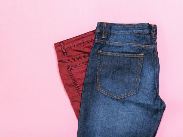 Blue jeans on top maroon on a pink background. The view from the top. Fashionable denim women's clothing. Denim women's clothing on colored background. Flat lay. - 写真・画像