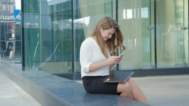 Young business woman talking is using smartphone in city park business center - Footage, Video