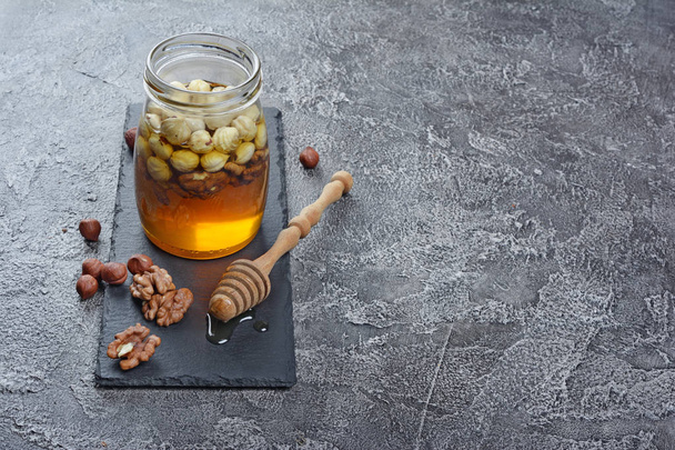 Healthy mix of natural honey with different nuts in a jar on gray concrete background - Foto, Bild