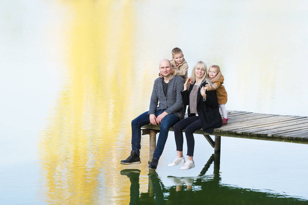 Onnellinen neljän hengen perhe istuu puulaiturilla lämpimänä syyspäivänä. Fall perheen muotokuva
 - Valokuva, kuva
