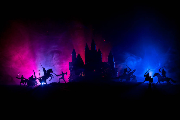 騎兵や歩兵との中世の戦闘シーン。中世の城と暗いトーン霧の背景に戦士の間で戦う、別のオブジェクトとしての人物のシルエット。選択的焦点 - 写真・画像