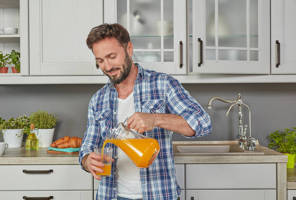 Uomo sano che beve succo d'arancia in cucina
 - Foto, immagini
