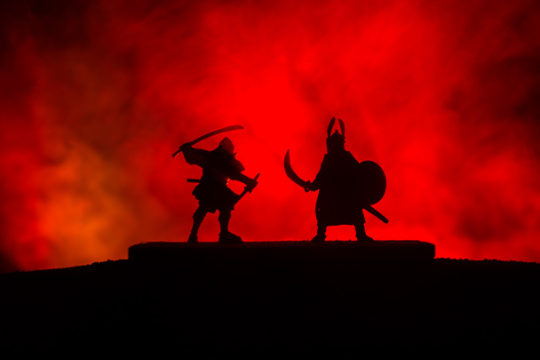 Silhouette of two medieval warriors in duel. Picture with two fighter with sword with dark toned foggy background. Selective focus. - Photo, Image