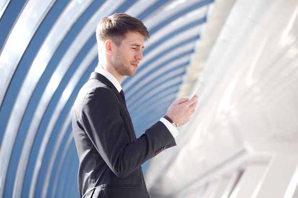 Businessman looking at his smartphone in modern building - Photo, Image