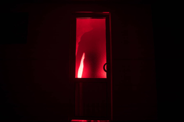 Silhouette einer unbekannten Schattenfigur auf einer Tür durch eine geschlossene Glastür. Die Silhouette eines Menschen vor einem Fenster in der Nacht. Gruselige Szene halloween Konzept der verschwommenen Silhouette von Wahnsinnigen. - Foto, Bild