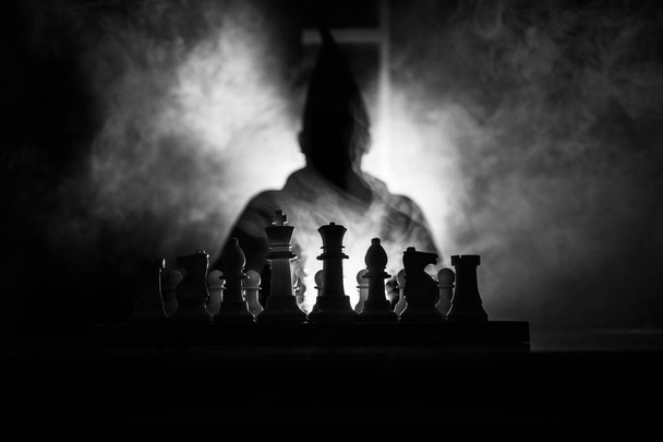 Man spelen schaak. Eng wazig silhouet van een persoon op het schaakbord met chess cijfers. Donker getinte mistige achtergrond. Selectieve aandacht. Horror concept - Foto, afbeelding