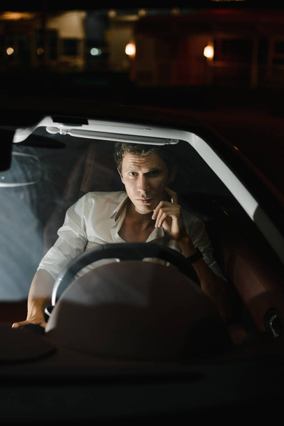 Front view. Portrait of a handsome man driving his car at night. The traffic lights behind him. - Foto, immagini