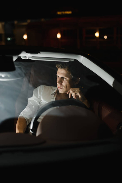 Handsome fashion man driving a car cabriolet. Luxury. Night life.The traffic lights behind him - Zdjęcie, obraz