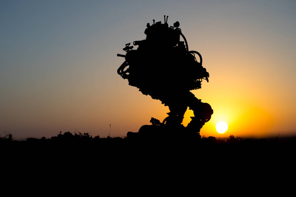 Σιλουέτα της γιγαντιαίο ρομπότ. Φουτουριστικό δεξαμενή σε δράση στο ηλιοβασίλεμα. Όχημα μάχης. - Φωτογραφία, εικόνα