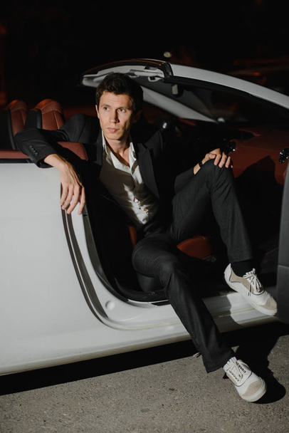 Portrait of a handsome man in white cabriolet. Nightlife. Businessman in suit in luxury car. - Fotó, kép