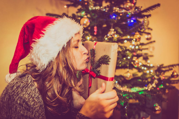 Chica Hipster con sombrero de santa. Mujer con un regalo cerca del árbol de Navidad. Tradición de dar regalos. Felices fiestas y celebraciones
. - Foto, imagen