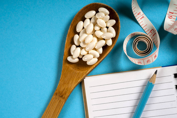 Foglio di piano di dieta e cucchiaio di legno con un nastro di misurazione su sfondo blu, dieta, stile di vita sano
. - Foto, immagini