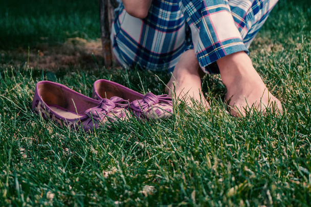 Barefoot harmony, girl sitting crosslegged on grass with her shes near - 写真・画像