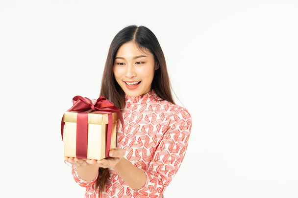 Photo of asian curious woman in red dress rejoicing her birthday or new year gift box. Young woman holding gift  box with red bow being excited and surprised  holiday present isolated white background - Foto, Bild