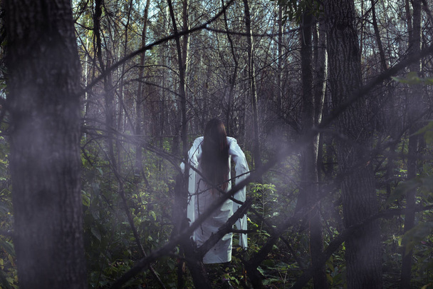 Portrait of a dead girl on Halloween in a gloomy forest. A ghost-girl in a gloomy dark forest at night on Halloween - Photo, Image