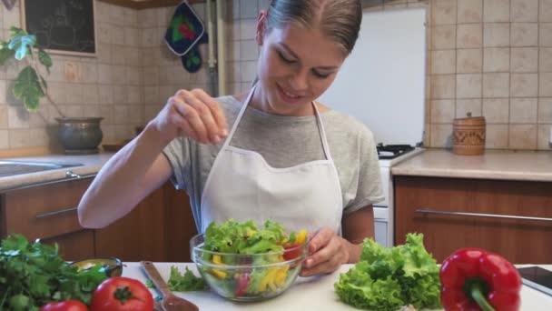 Jeune femme en salade d'assaisonnement tablier. Femme au foyer préparant le dîner végétarien à la maison
. - Séquence, vidéo