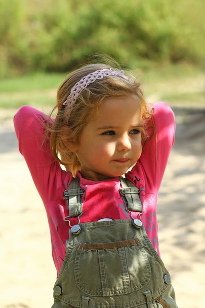 屋外の頭の後ろに手をポーズ ピンクのかわいい太陽に照らされた幼児の女の子 - 写真・画像