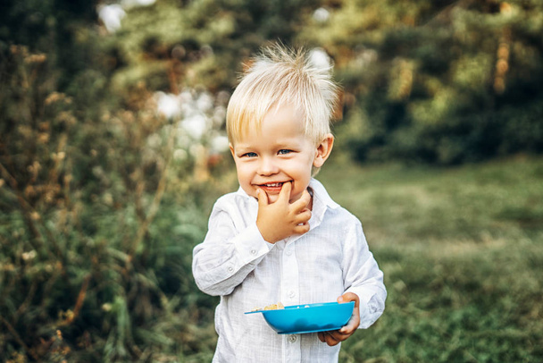 Cute little baby boy holding bowl with food while having fun outdoor - Foto, Bild