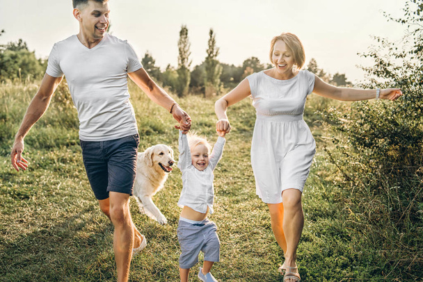 Happy young parents holding hands little son having fun with dog outdoor - Foto, imagen