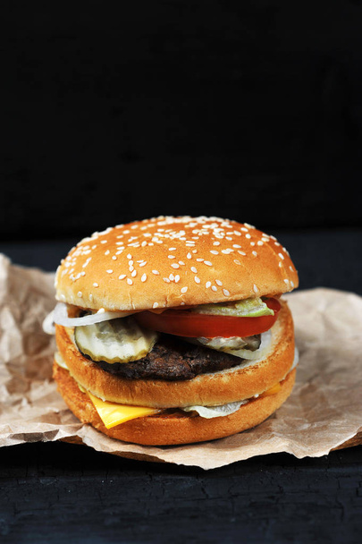 fast food-cut in half or bitten Burger with cheese and beef on Kraft paper on black charcoal background - Photo, image