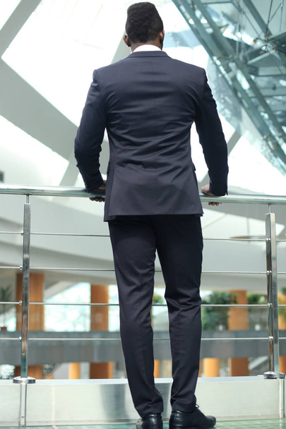 Vista posteriore di uomo d'affari afroamericano in giacca e cravatta in attesa, in edificio per uffici
. - Foto, immagini