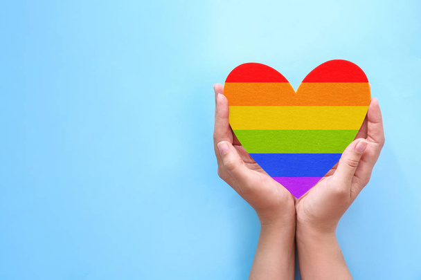 Woman holding heart painted in LGBT flag colors and space for text on blue background. Gay pride - Foto, Imagen