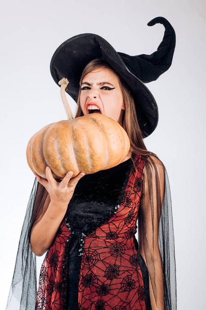 Cute girl in witch costume on wall background. Halloween Party girl. Beautiful young surprised woman in witches hat and costume holding pumpkin. - Fotografie, Obrázek