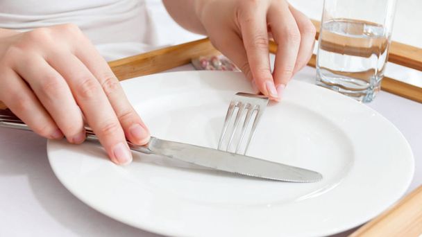 Closeup photo of sick woman lying in bed holding fork and knife over empty dish. Concept of diet and loosing weight - Photo, Image