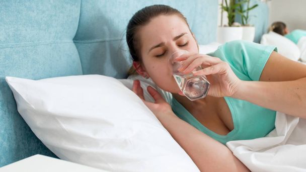 Πορτρέτο του νεαρή γυναίκα ξαπλωμένη στο κρεβάτι μια πόσιμου νερού από γυαλί - Φωτογραφία, εικόνα