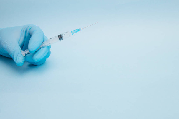 Female hand holding syringe with blue background. - Zdjęcie, obraz